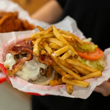 A person holding a basket of food with fries and bacon.