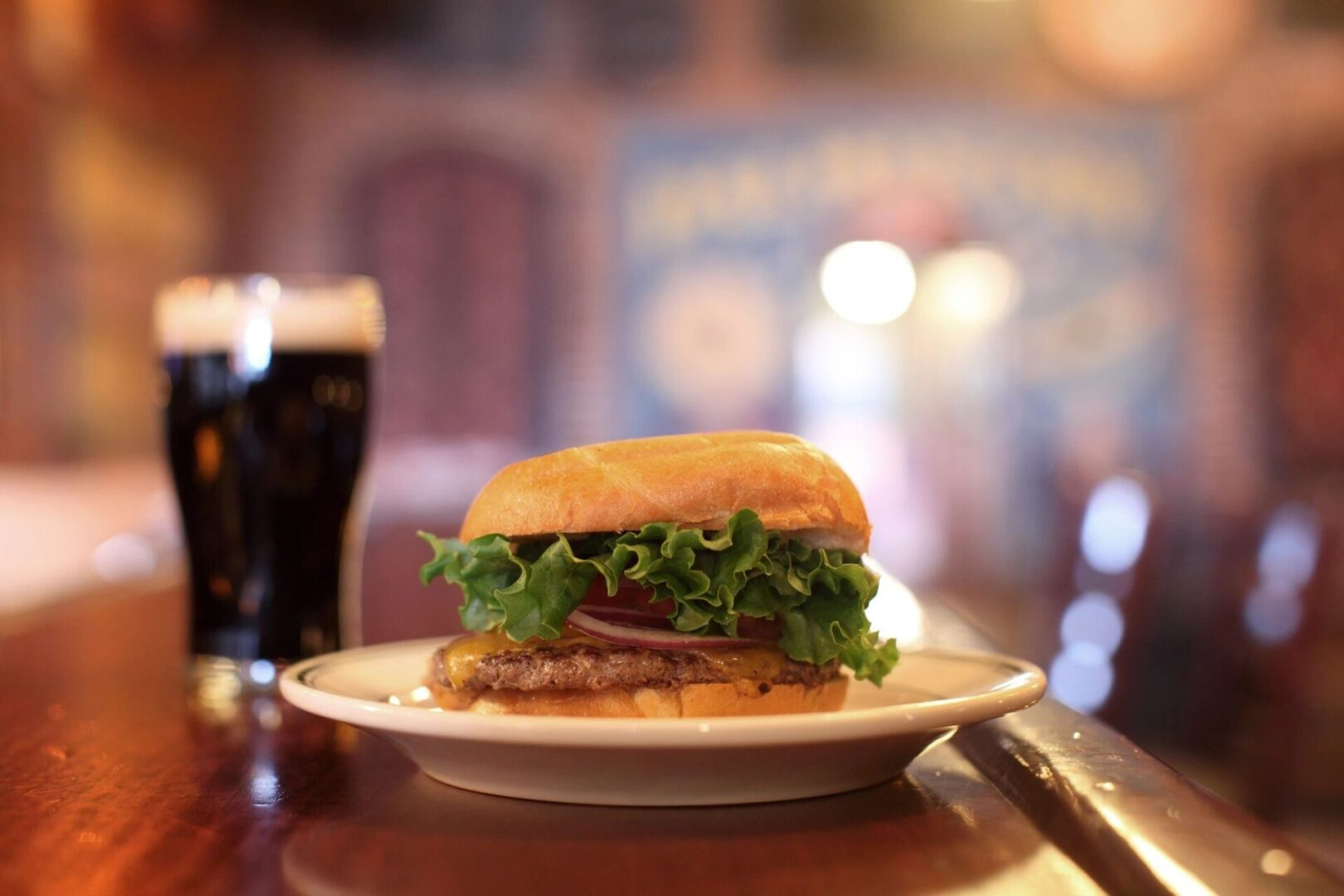 A sandwich on a plate with a glass of beer in the background.