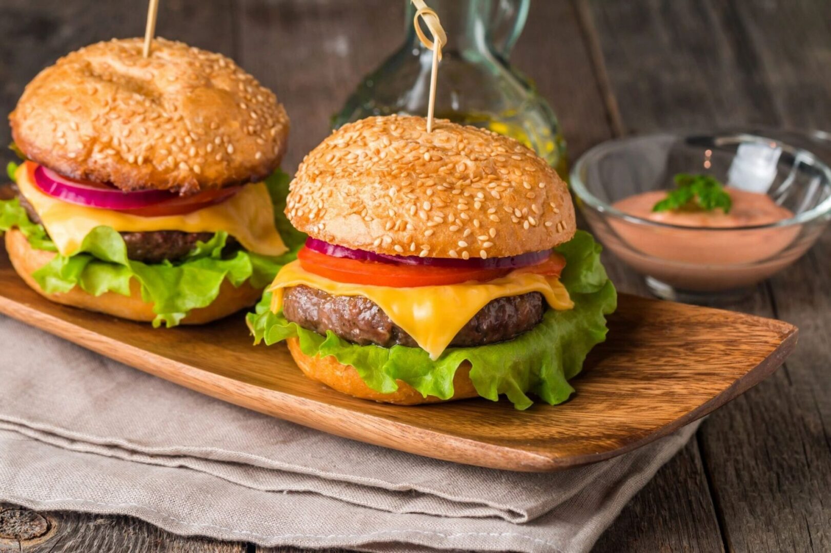 Two hamburgers on a wooden board with ketchup and mustard.