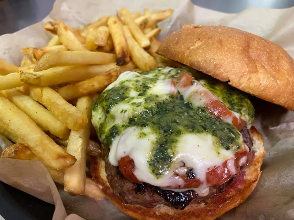 A hamburger with cheese and pesto next to fries.